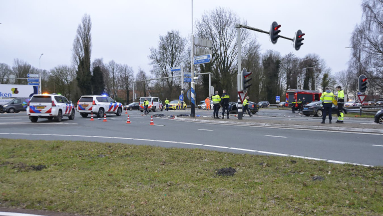 Auto-ongeluk op een kruispunt, met een beschadigde auto, verspreide brokstukken en politie ter plekke.