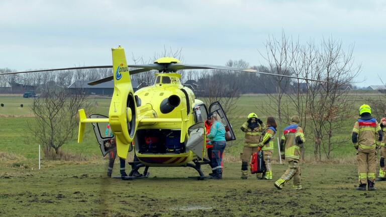 Hulpdiensten, waaronder brandweerlieden en medisch personeel, werken samen in een veld bij een boerderij.