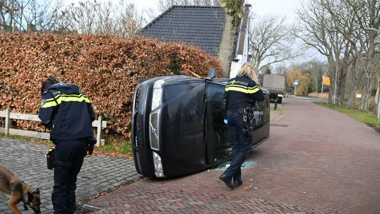 Politieagenten staan bij een geparkeerde auto voor een supermarkt, met een politiewagen op de achtergrond.