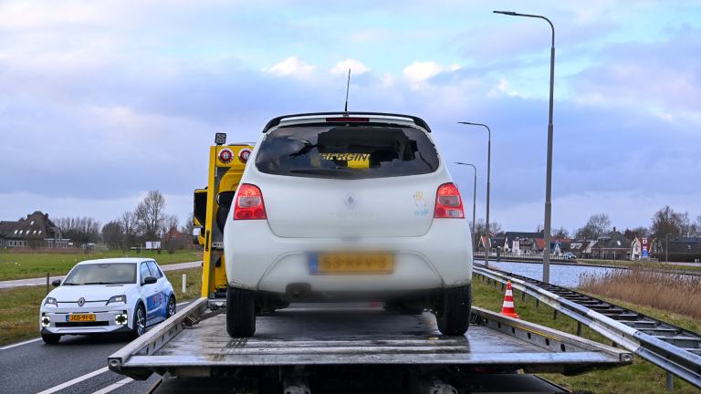 Rode vrachtwagen van Lubbers met lange oplegger en container, geparkeerd langs een weg met gebouwen en een molen op de achtergrond.