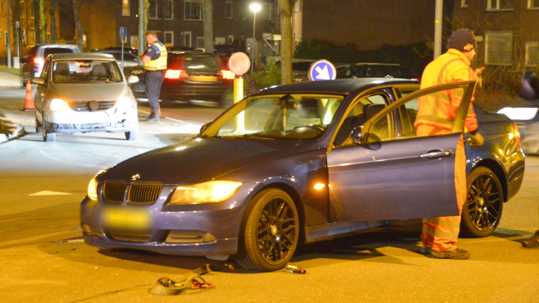 Auto-ongeluk bij nacht op kruispunt, met schade aan twee voertuigen; man in veiligheidskleding onderzoekt de situatie.