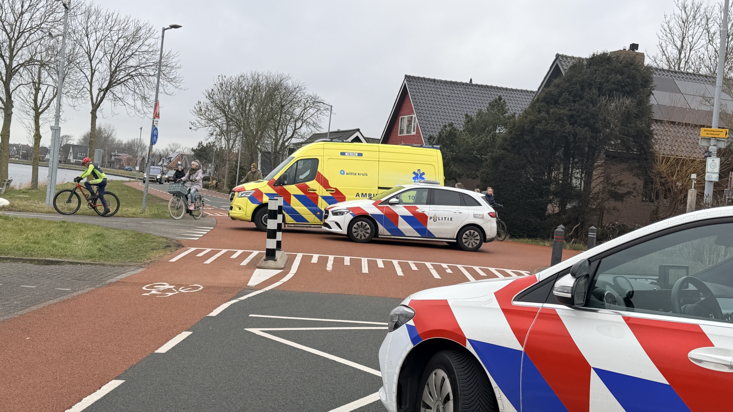 Auto met gebarsten voorruit en liggende fiets op fietspad, agent op de achtergrond.