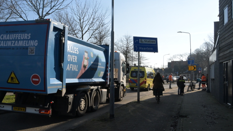 Een geparkeerde fiets op de stoep voor een ambulance en verkeersbord met een politieagent op de achtergrond.