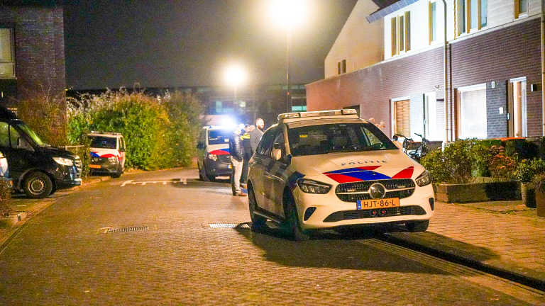 Politieauto's geparkeerd op een straat 's nachts, met meerdere mensen die naast een voertuig staan praten.