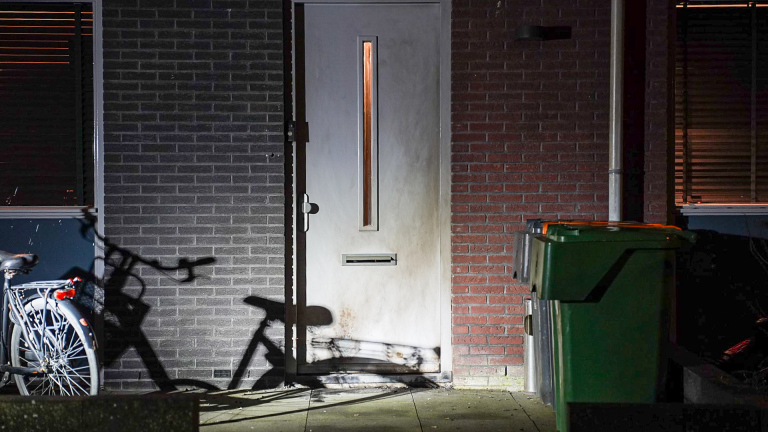 Politieauto's geparkeerd op een straat 's nachts, met meerdere mensen die naast een voertuig staan praten.