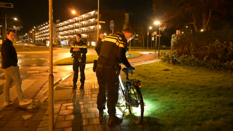 Politieagenten controleren 's nachts een fiets op een troittoir; een man kijkt toe.