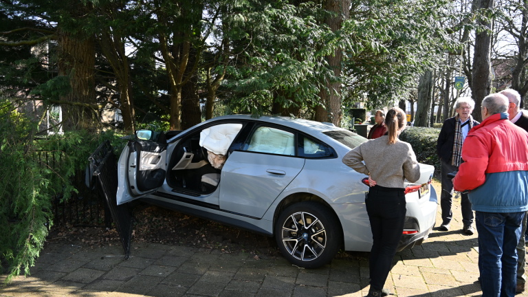 Een zilveren auto is tegen een boom gereden met de airbags uitgeklapt; enkele mensen staan er omheen te kijken.