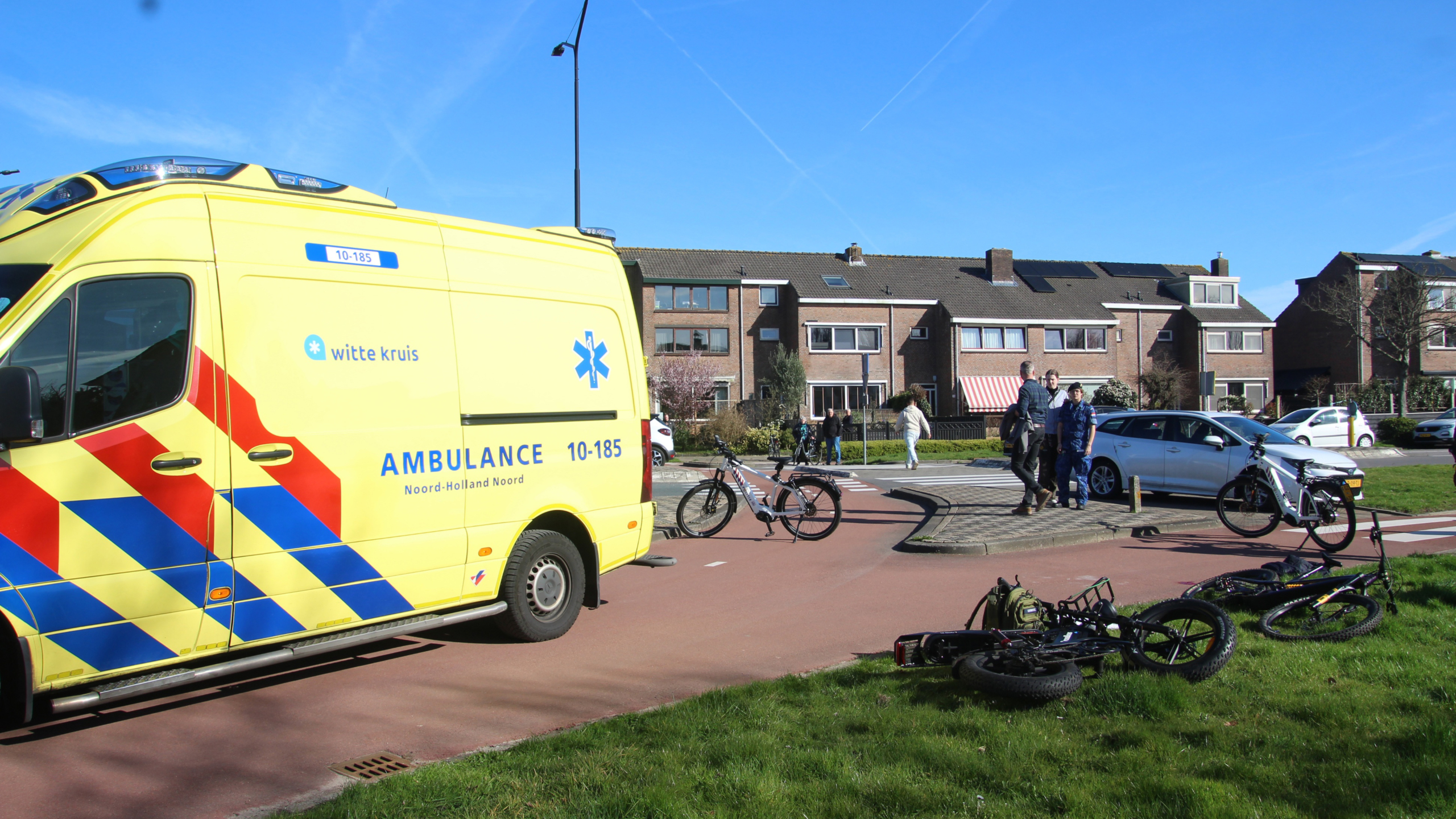 Mensen helpen een persoon op een brancard bij een ambulance, met een geopende achterdeur in een stedelijke omgeving.