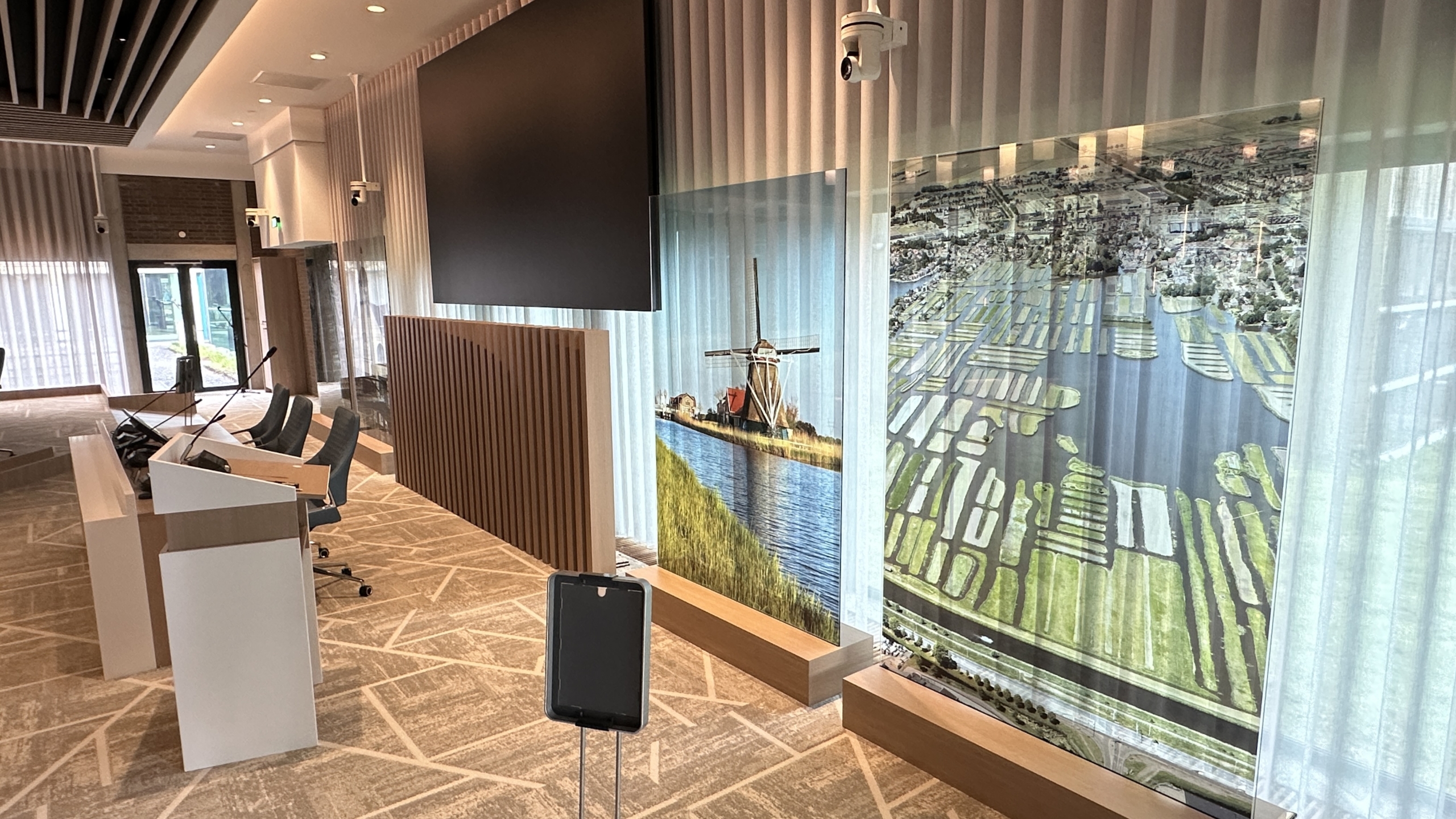 Vergaderzaal met rondom een grote ovale tafel, blauwe stoelen en moderne hanglampen aan het plafond.