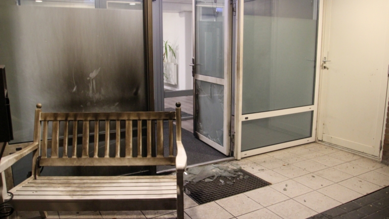 Bankje en gebroken glazen deur in een beschadigde hal met roet op het raam.