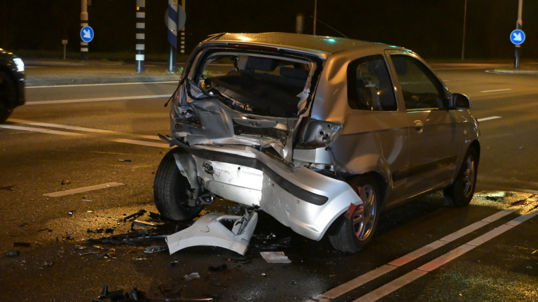 Verkeersongeluk in de nacht bij een kruispunt; ambulance en verschillende auto's aanwezig met politie en verkeerslichten op groen.