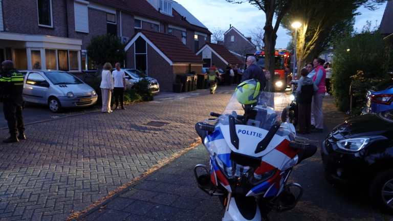 Politiemotor en agent op straat tijdens een avondlijke situatie met publiek en een brandweerwagen op de achtergrond.