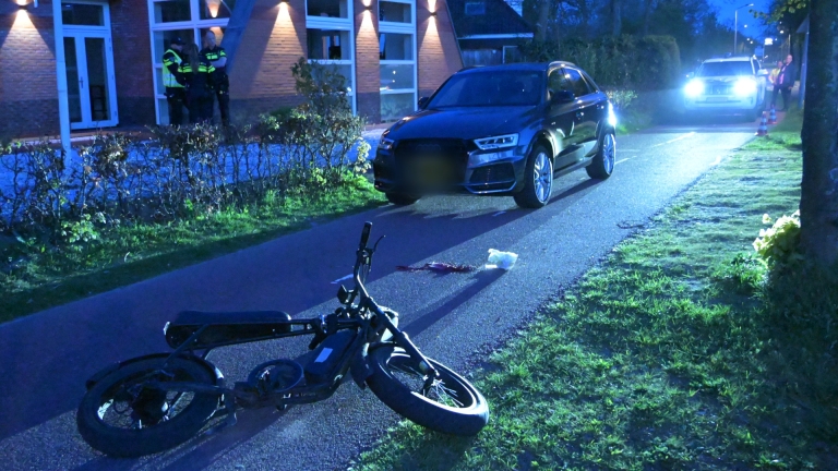 Agenten begeleiden een persoon naar een politieauto in het schemerlicht langs een rustige weg.