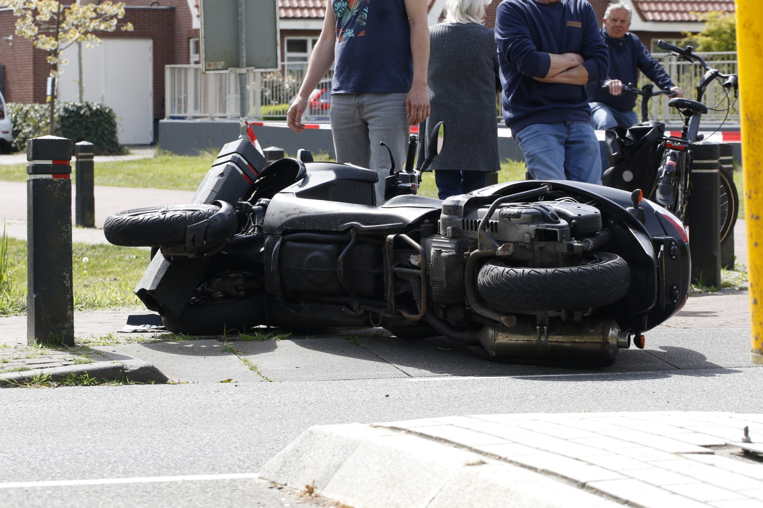 Politievoertuig en motorkap bij afzetting op straat; politieagenten staan bij een groot gebouw.