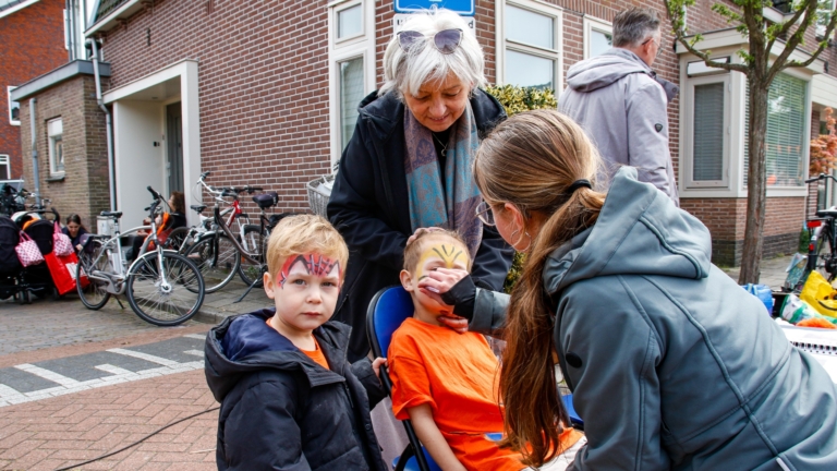 Mensen lopen langs een drukke markt met kraampjes en een Nederlandse vlag, nabij een historische kerk en gebouwen.