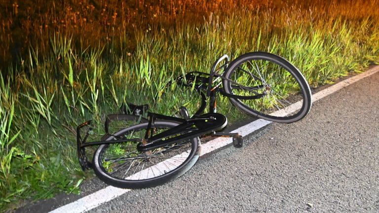 Twee politieagenten en een omgevallen scooter langs de weg bij nacht, met een ambulance op de achtergrond.
