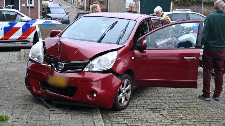 Agenten praten met een man naast een rode auto; een politiefiets met blauwe en rode strepen staat op de voorgrond.