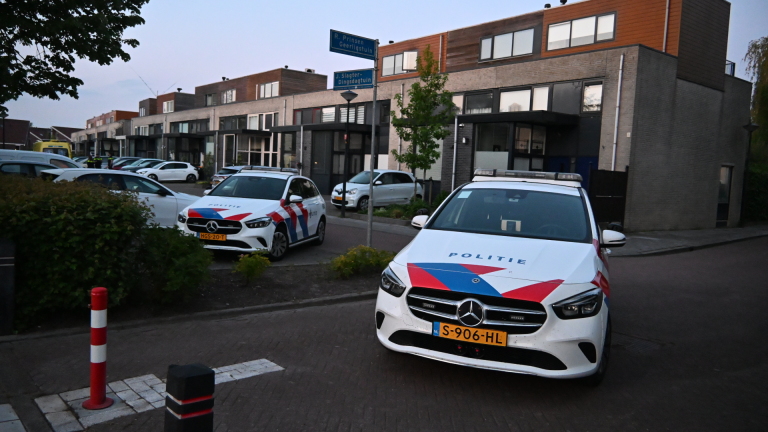 Twee politieauto's geparkeerd in een woonwijk bij moderne huizen, met straatnaamborden op de achtergrond.