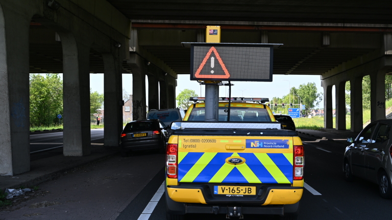 Politiecontrole onder viaduct met agenten in reflecterende kleding, een politie-motorfiets en passerende auto's.