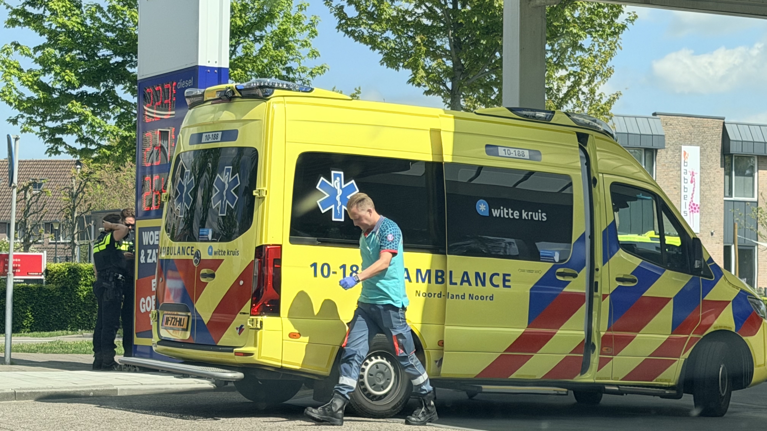 Auto met ingedeukt voorpaneel en gebarsten voorruit, geparkeerd bij een tankstation op een zonnige dag.