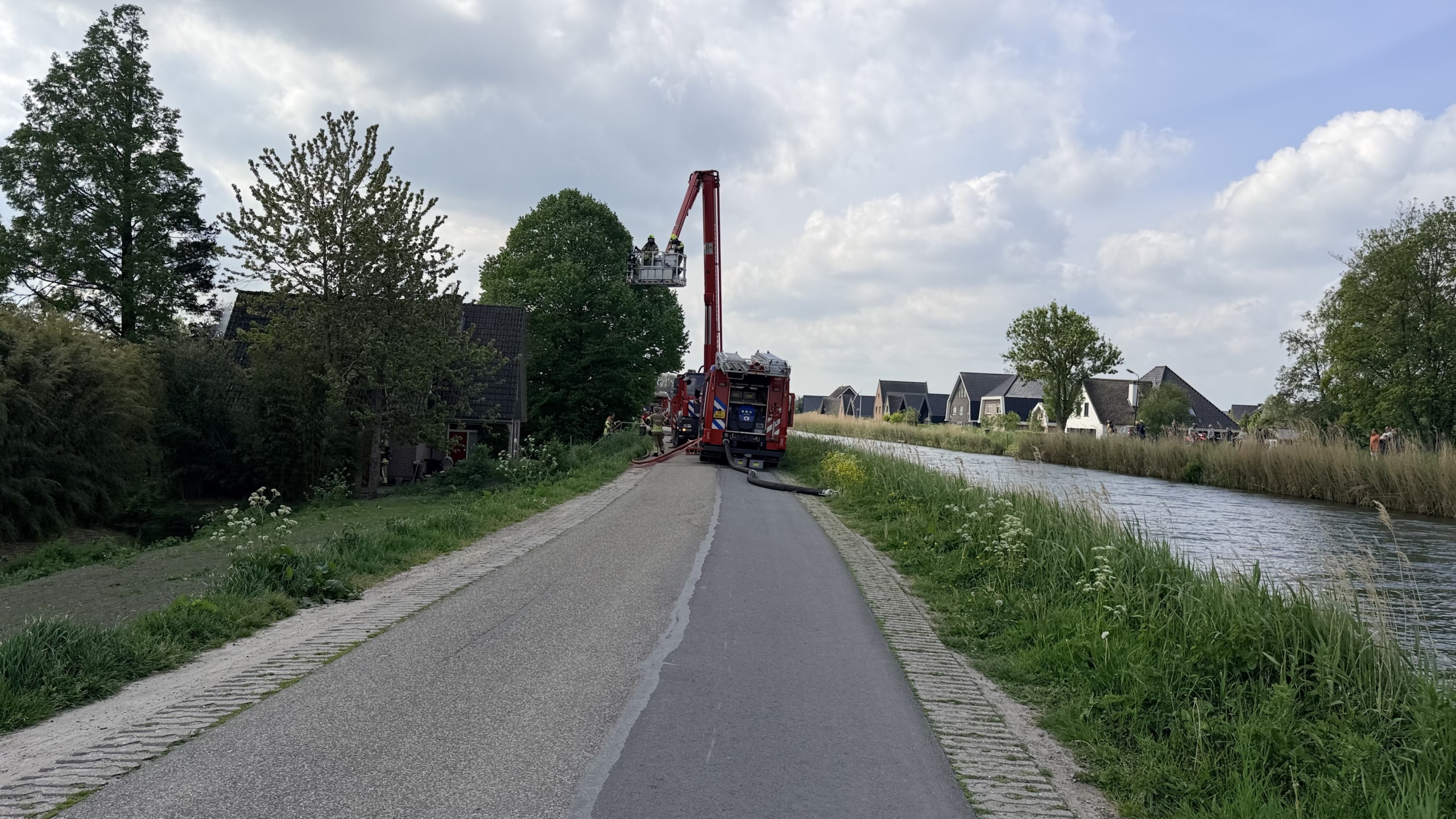 Brandweerlieden bestrijden brand in een huis met een gebroken raam en rook uit het dak, ondersteund door een hoogwerker.
