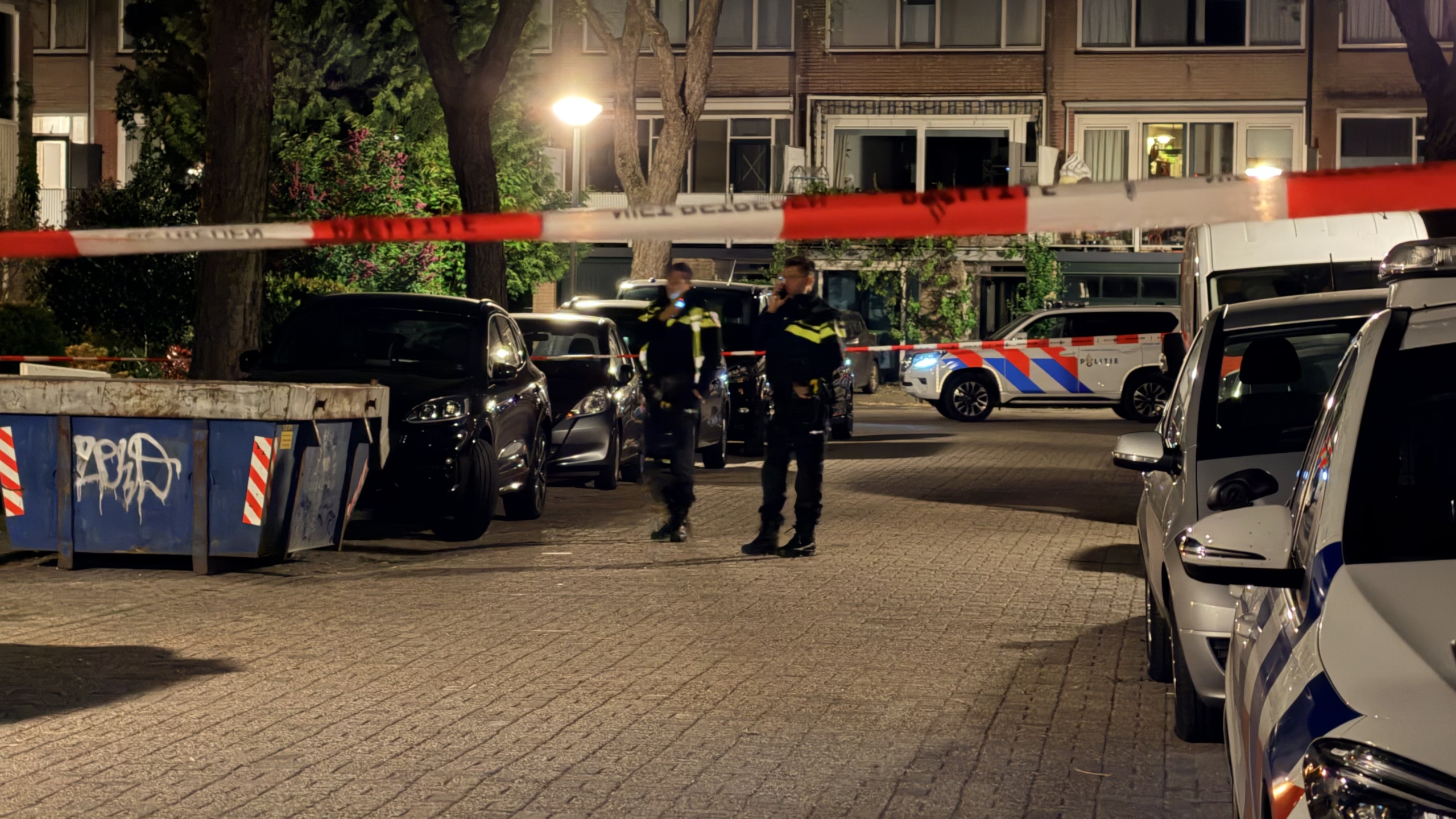 Twee politieagenten staan 's nachts voor een huis, kijkend naar de voordeur met een fiets op de grond.