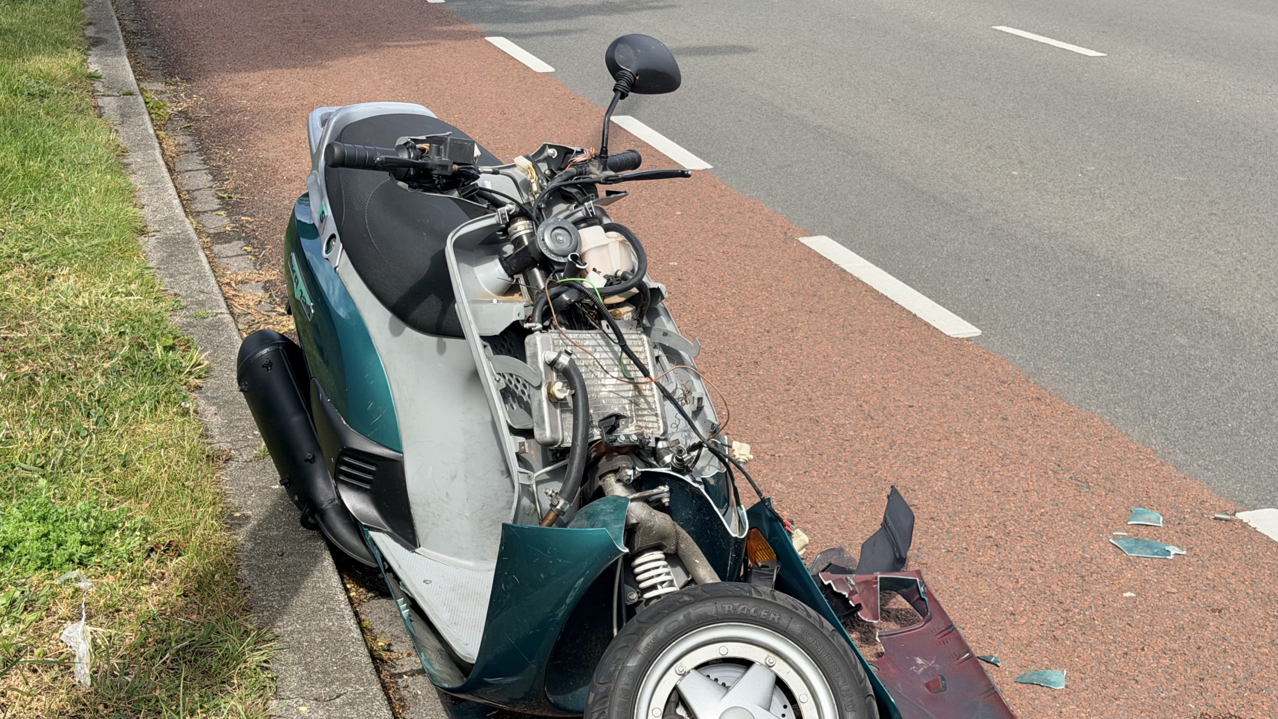 Hulpdiensten helpen een gewonde persoon op een brancard bij een ongeval op straat; een ambulance staat klaar.