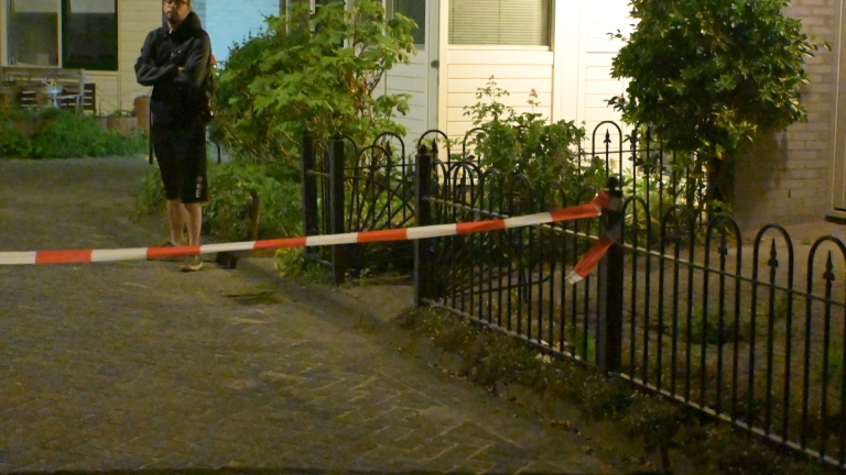 Tuin omheind met rood-wit lint bij nacht, man staat naast een huis met gesloten jaloezieën.