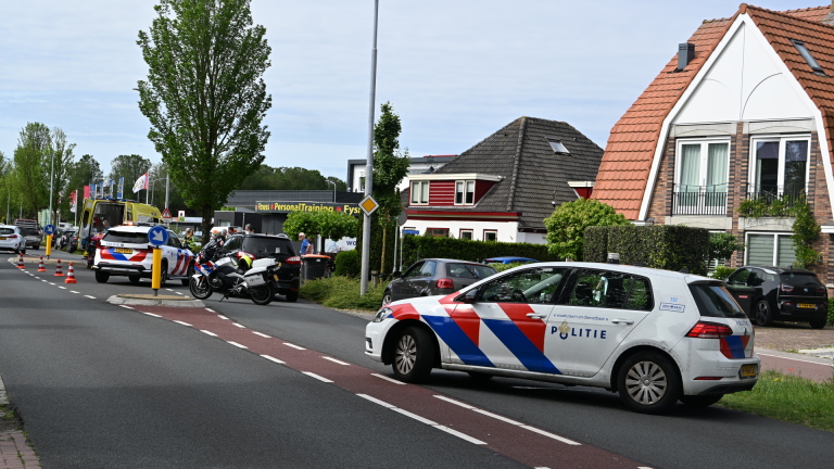 Politieauto en ambulance bij een incident, met hulpverleners en omstanders op straat.