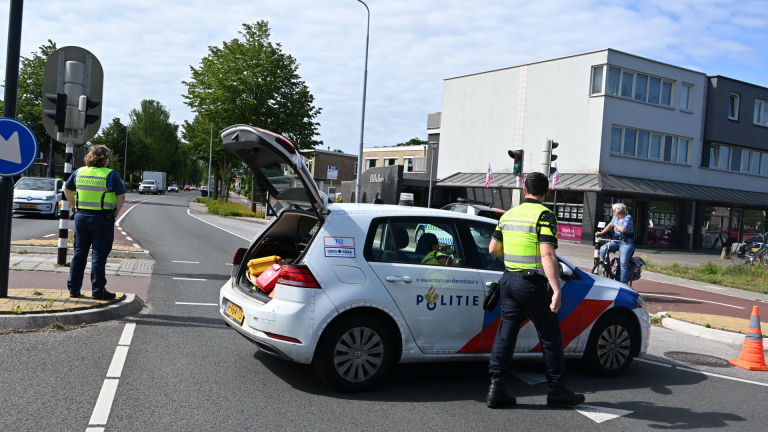 Politieauto en ambulance bij een incident, met hulpverleners en omstanders op straat.