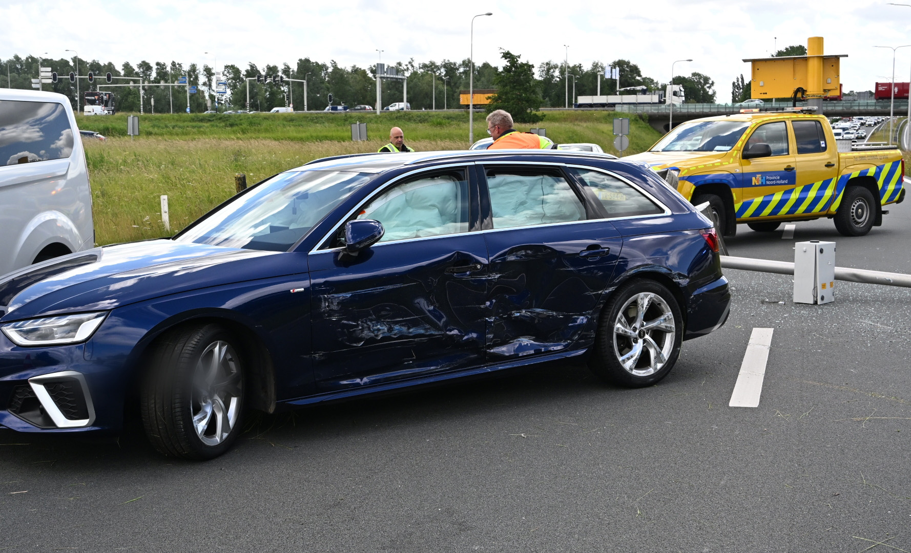 Twee beschadigde auto's en een omgevallen verkeerspaal op de weg, omgeven door mannen in fluorescerende kleding.