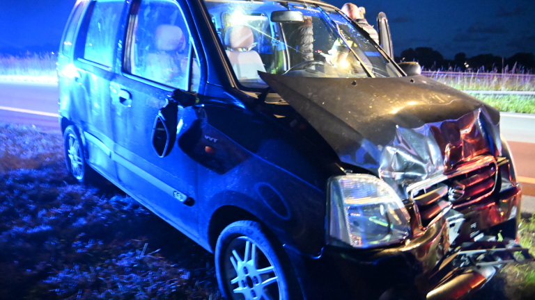 Ambulance met geopende deuren langs de weg in de schemering, naast een auto en verkeersbord.