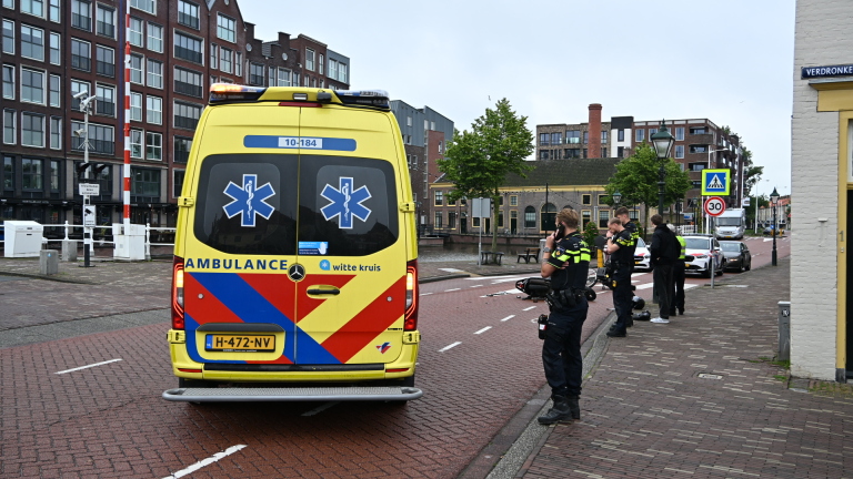 Omgevallen scooter en fiets op de weg naast politieauto's in een stedelijke omgeving.