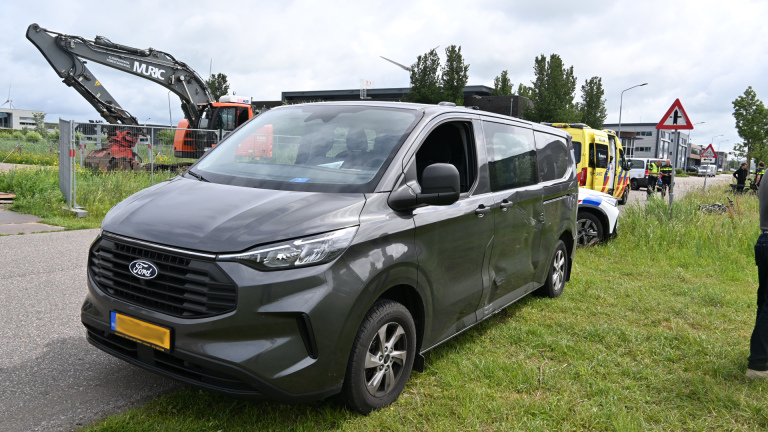 Een grijze bestelwagen staat geparkeerd naast een bouwterrein met een graafmachine, naast een ambulance en agenten.