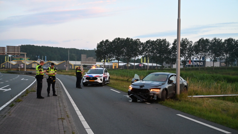 Een auto met ernstige schade aan de voorkant staat tegen een lantaarnpaal langs de weg.