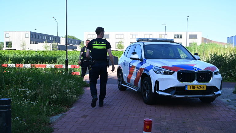 Een politieauto met rode en blauwe strepen staat geparkeerd voor een bakstenen gebouw.