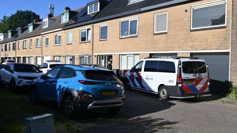 Een politieauto met rode en blauwe strepen staat geparkeerd voor een bakstenen gebouw.