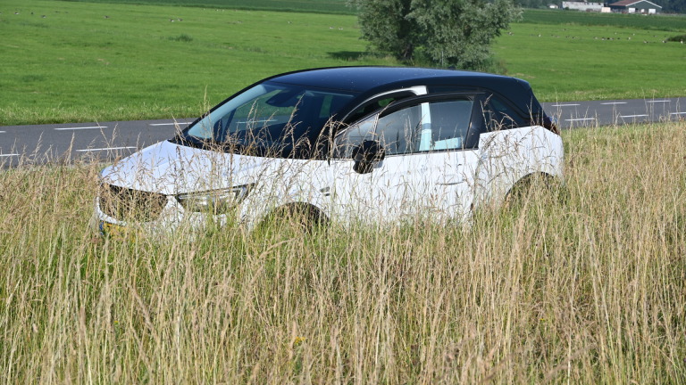 Beschadigde witte auto naast vangrail, met twee mannen in oranje werkkleding dichterbij op de weg.