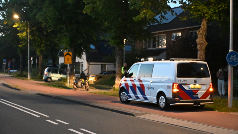 Een politiebus geparkeerd langs een weg bij een fietspad in een wijk, met bomen en huizen op de achtergrond.