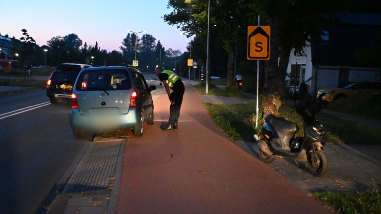 Een politiebus geparkeerd langs een weg bij een fietspad in een wijk, met bomen en huizen op de achtergrond.