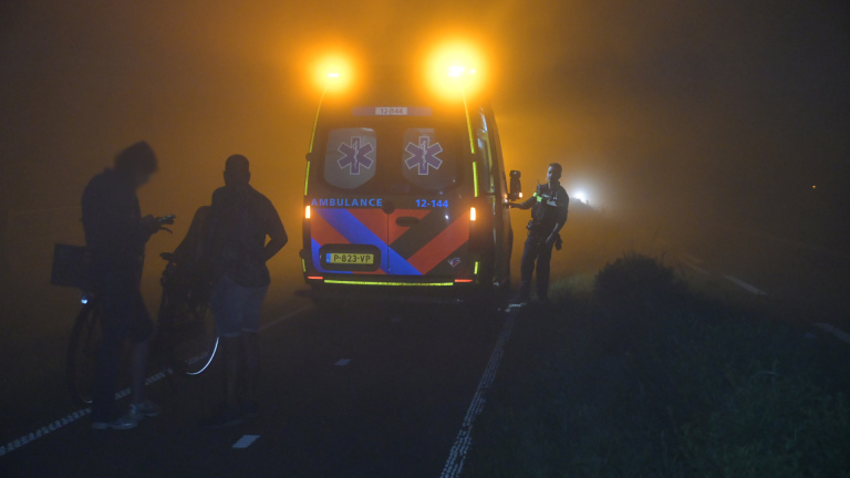 Hulpverleners en politie bij een ambulance op een donkere weg, klaar om een brancard in te laden.