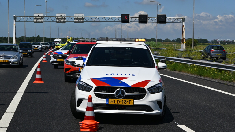 Hulpverleners op de snelweg bij een ongeval, naast een beschadigde auto en een afgebroken aanhanger.