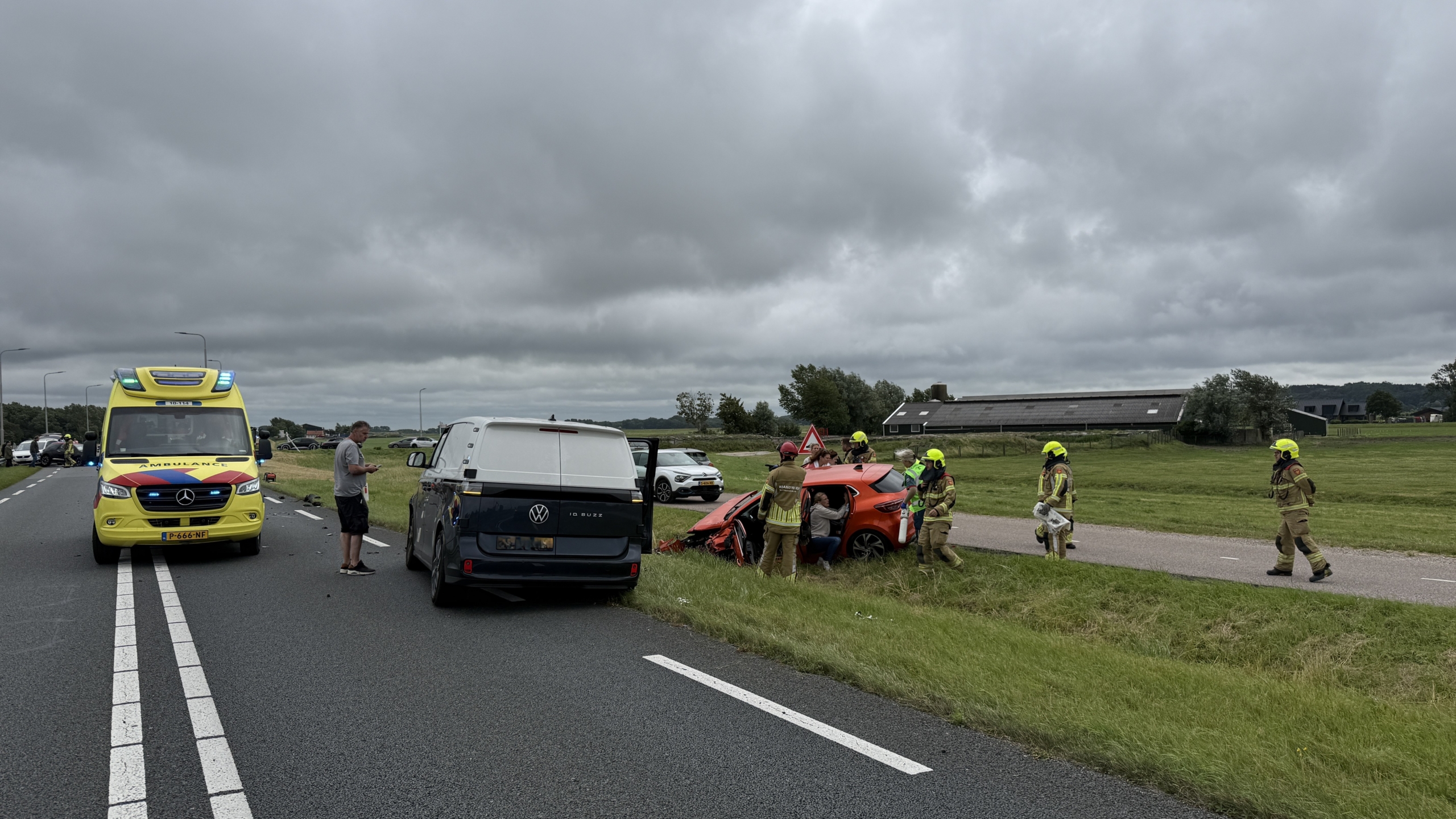 Verkeersongeval op een snelweg met betrokken auto's, brandweerlieden en twee ambulances aanwezig, omstanders kijken toe.