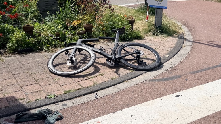 Zwarte racefiets ligt op de stoep naast een fietspad en zebrapad, met een doek op de weg en planten op de achtergrond