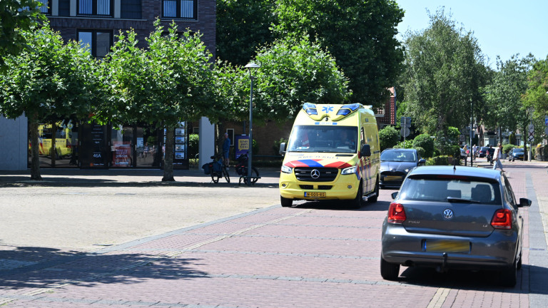 Twee politieagenten lopen langs een geparkeerde politieauto op een straat met bomen en woonhuizen