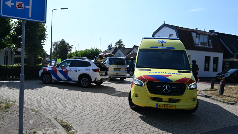 Politieagent loopt naast een vrouw die haar vouwfiets duwt op straat tussen geparkeerde auto’s