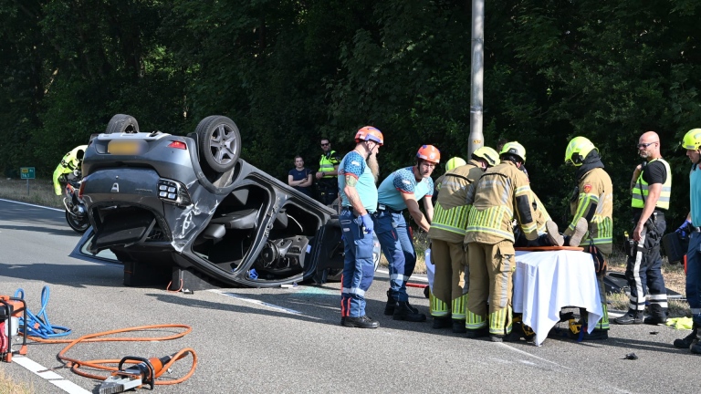 Hulpdiensten en politie bij een ongeval op de weg, met een auto die op zijn dak ligt en een brancard ernaast