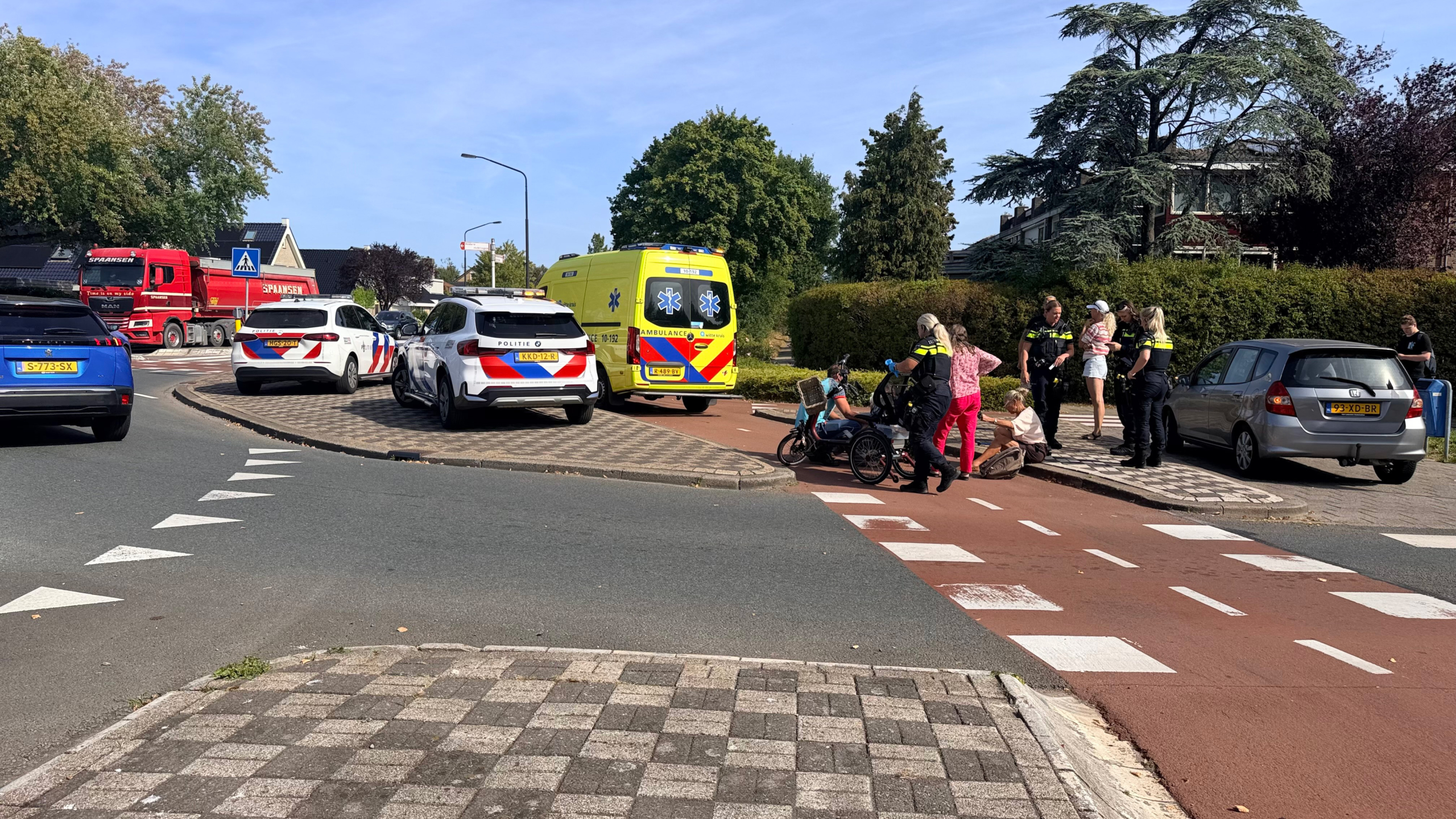 Driewieler met lage instap, mandje voorop en rugleuning, geparkeerd op een fietspad bij een kruising