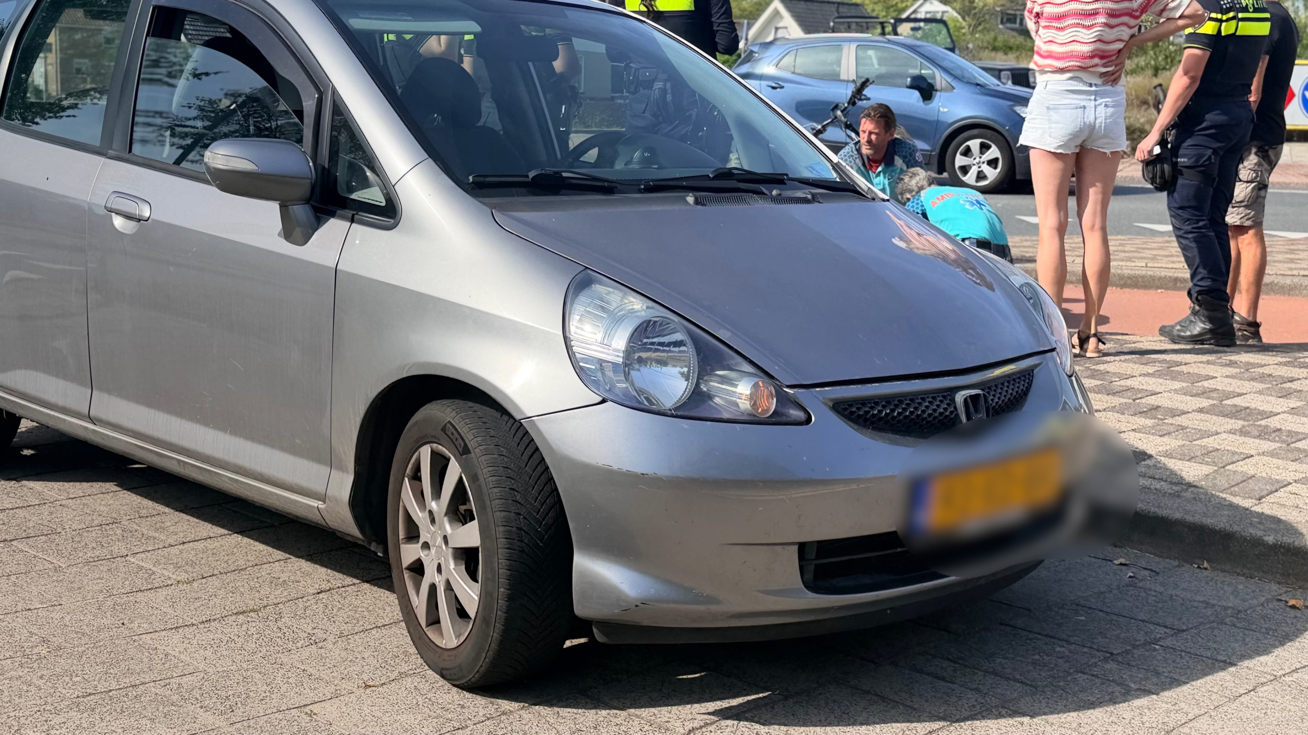 Driewieler met lage instap, mandje voorop en rugleuning, geparkeerd op een fietspad bij een kruising