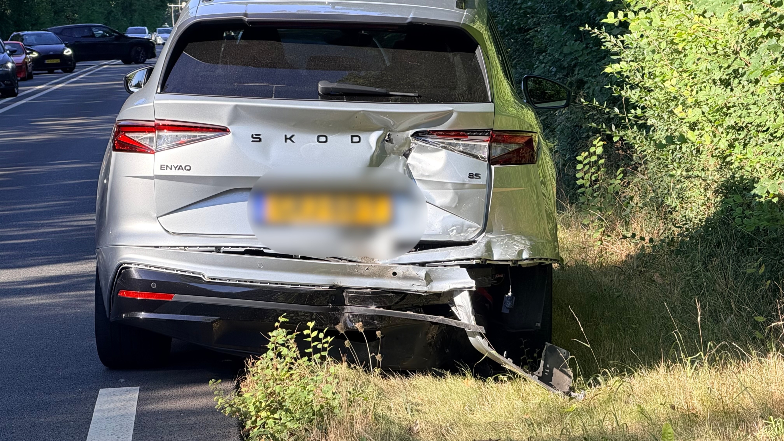 Ambulance en politie bij auto-ongeluk op bosrijke weg, met beschadigde zwarte auto en brokstukken op het asfalt